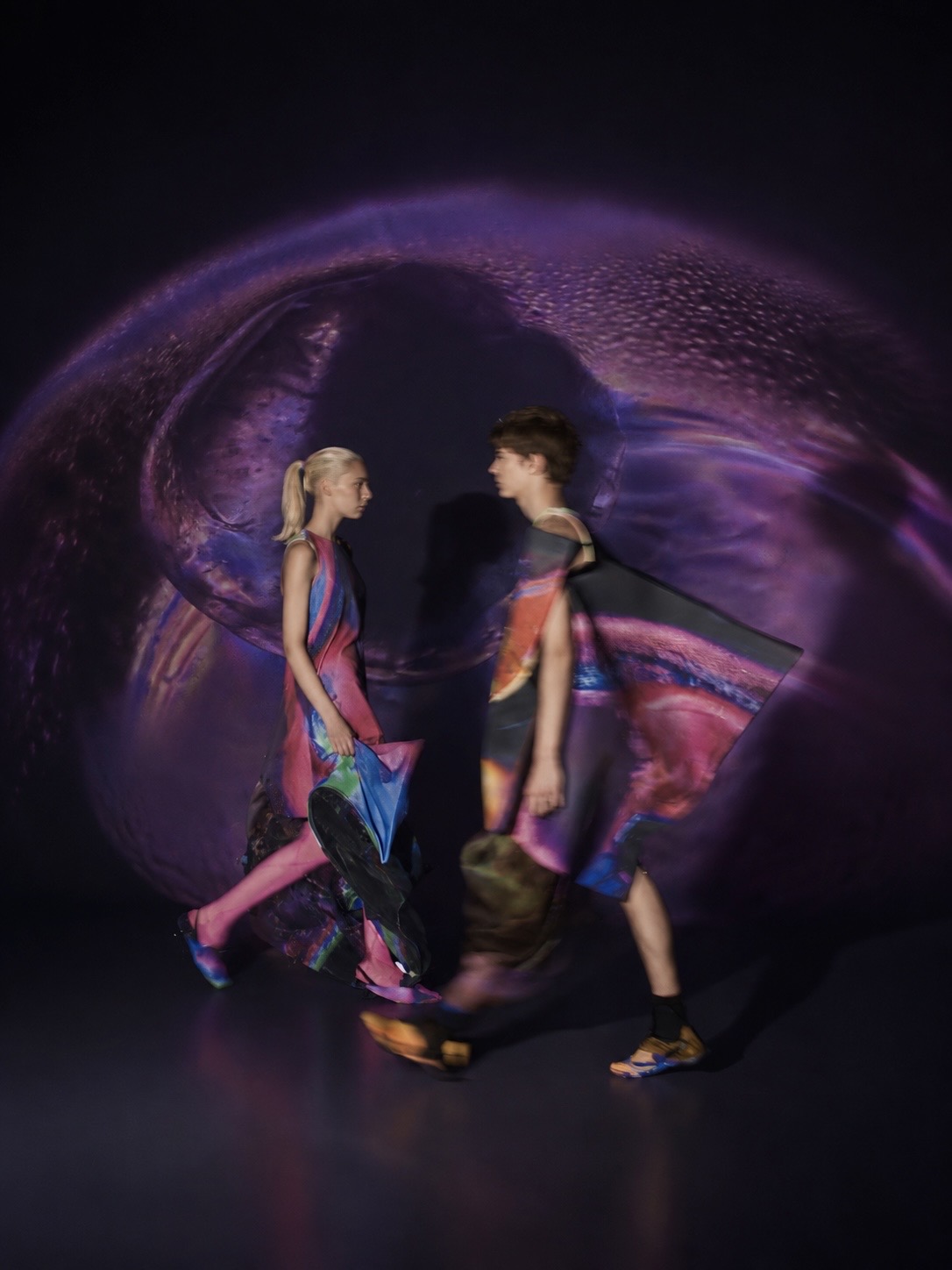 Two models passing one another inside a soft violet halo